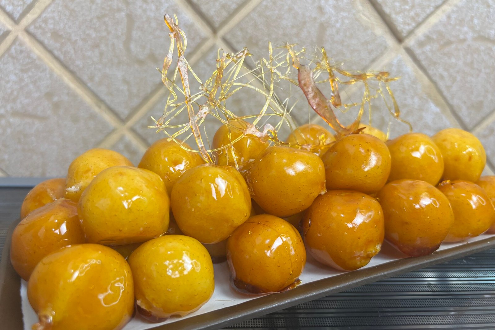 Brazilian bala baiana coconut balls coated in shiny caramel with decorative sugar threads on a white plate