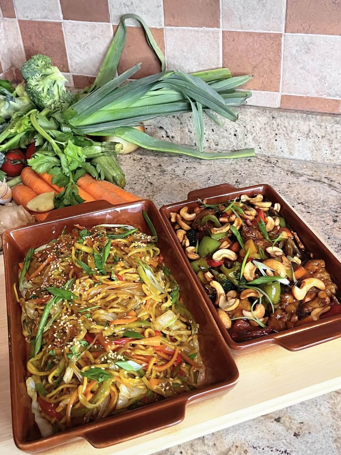 Bowls of vegetable noodles and chicken cashew stir fry garnished with sesame seeds and green onions