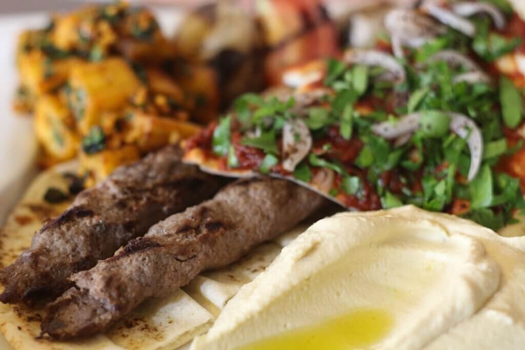Traditional Lebanese mezze platter with hummus, grilled kafta kebabs, roasted vegetables, fresh herbs, and flatbread served on a large plate.