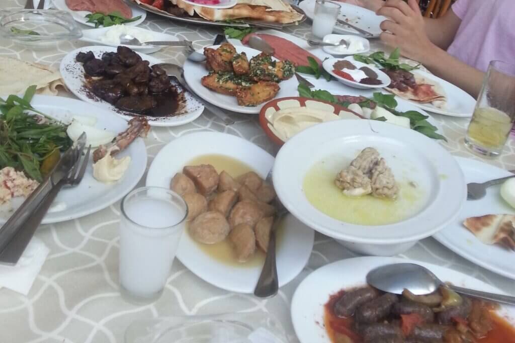 Traditional Lebanese cuisine table with hummus, grilled meats, kibbeh, sausages, fresh herbs, yogurt dishes, and assorted Middle Eastern appetizers served family style.