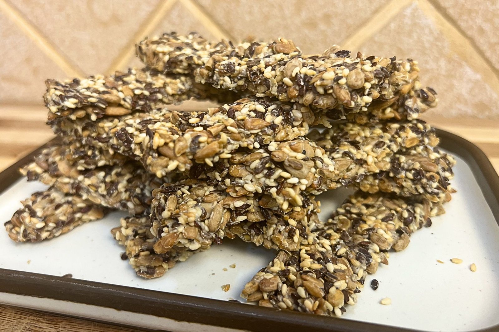 Close-up of homemade gluten-free seeds crackers stacked on a white plate, made with sunflower seeds, flaxseeds, and sesame seeds, showing a crispy crunchy texture.