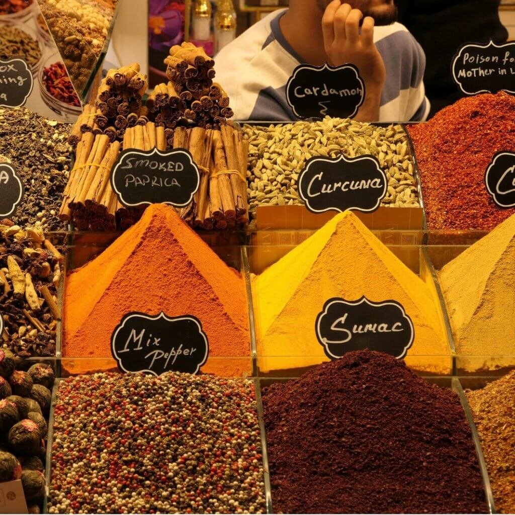 Colorful spice display in a Middle Eastern market featuring fresh ground sumac, paprika, turmeric, cardamom, cinnamon sticks, and mixed pepper.