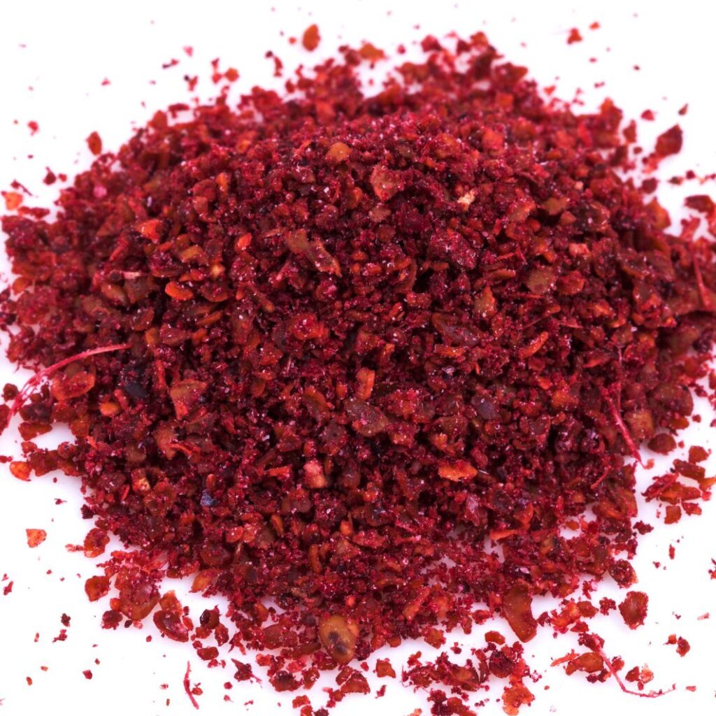 Close-up of freshly ground dark red sumac spice with a coarse texture on a white background.