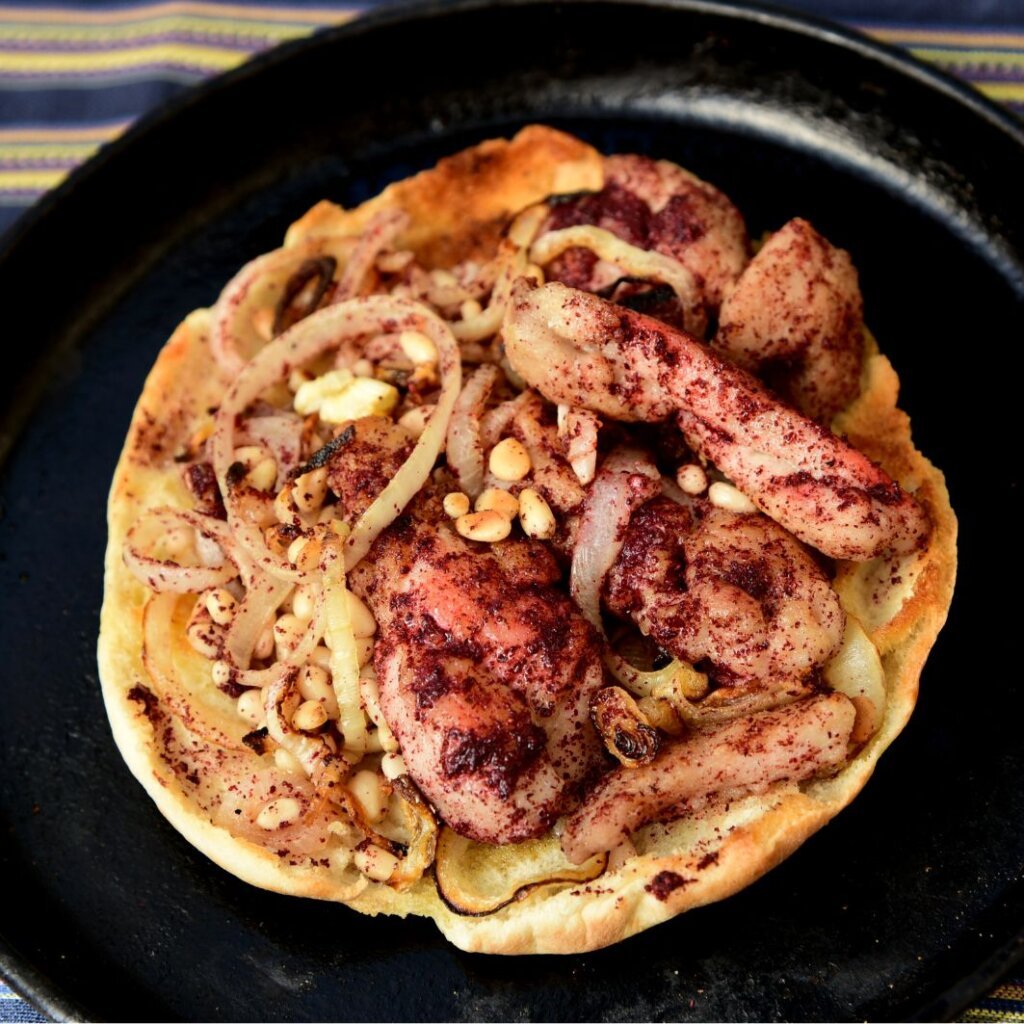 Traditional Palestinian and Lebanese chicken musakhan topped with sumac, caramelized onions, and pine nuts on flatbread.