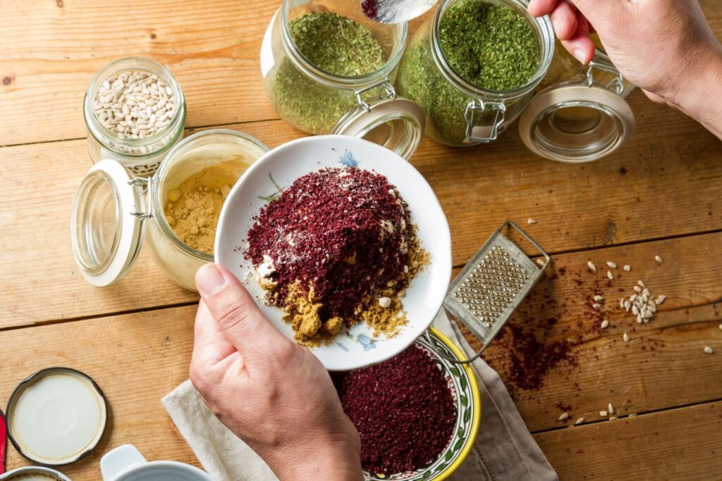 Hands preparing a traditional Middle Eastern spice blend with freshly ground sumac, herbs, and seeds on a wooden table.