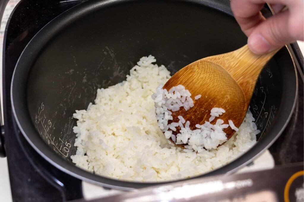 Wooden spoon stirring sticky white rice inside a cooking pot