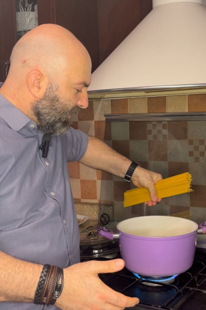 Chef François adding spaghetti into a pot of boiling water in a home kitchen while preparing pasta.