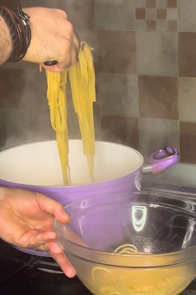 Close-up of spaghetti being lifted from boiling water into a glass bowl during pasta preparation.