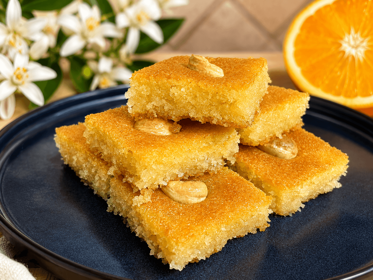 Golden pieces of Lebanese nammoura stacked on a dark plate, topped with almonds and soaked in fragrant orange blossom syrup.