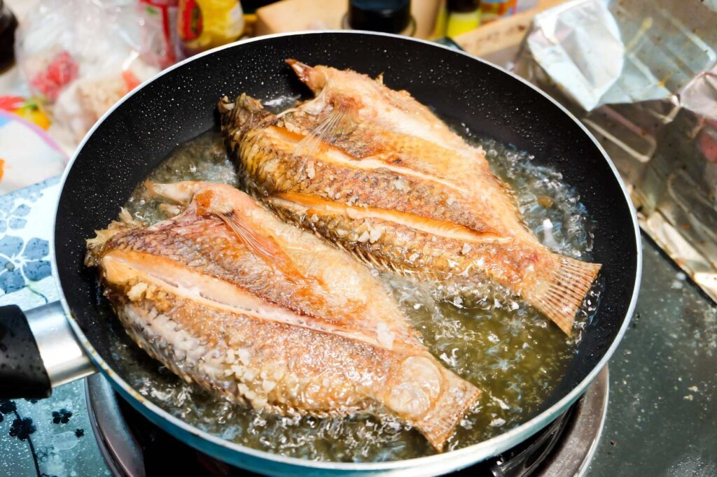 Two whole fish frying in hot oil in a skillet, illustrating common mistakes that can affect crispy skin and even cooking.