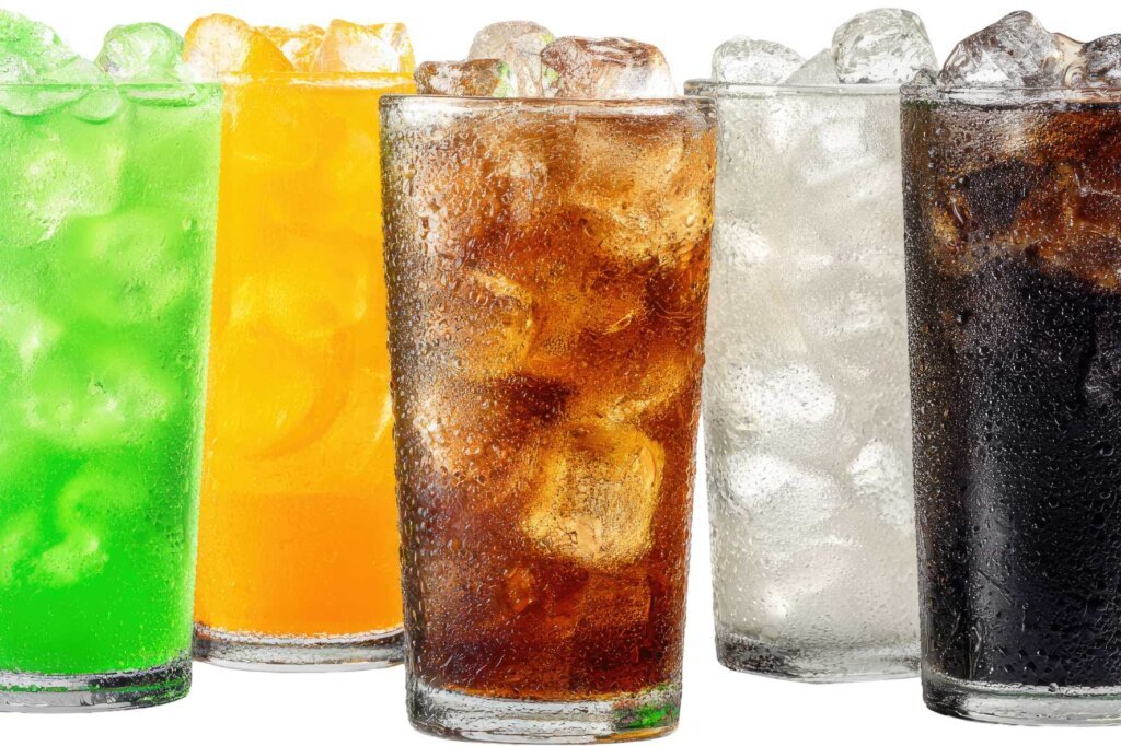 A selection of ice-cold soft drinks in tall glasses filled with ice cubes, commonly served alongside crispy fried foods and fast-food meals.