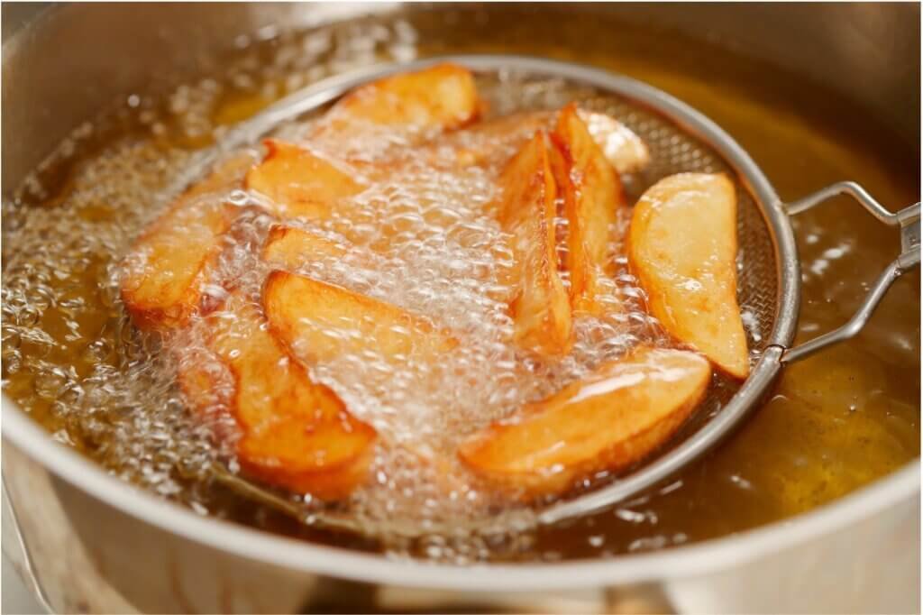 Golden potato wedges frying in clean, fresh cooking oil with vigorous bubbles, demonstrating the importance of using new oil for crispy fried food.