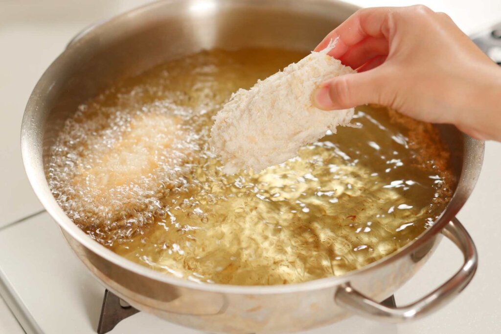 A breaded chicken fillet being lowered into hot oil for frying, illustrating common mistakes that can affect crispiness and cause the coating to fall off.