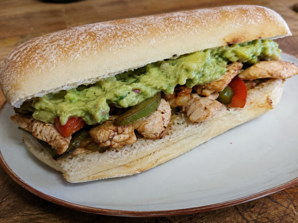 Chicken guacamole sandwich made with grilled chicken fajita filling and creamy guacamole served in soft samoli bread on a plate.