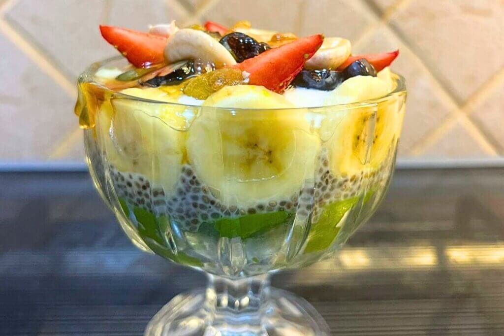 Berry-Cado chia cup layered with avocado, chia pudding, banana, strawberries, blueberries, cashews, and honey in a glass dessert bowl