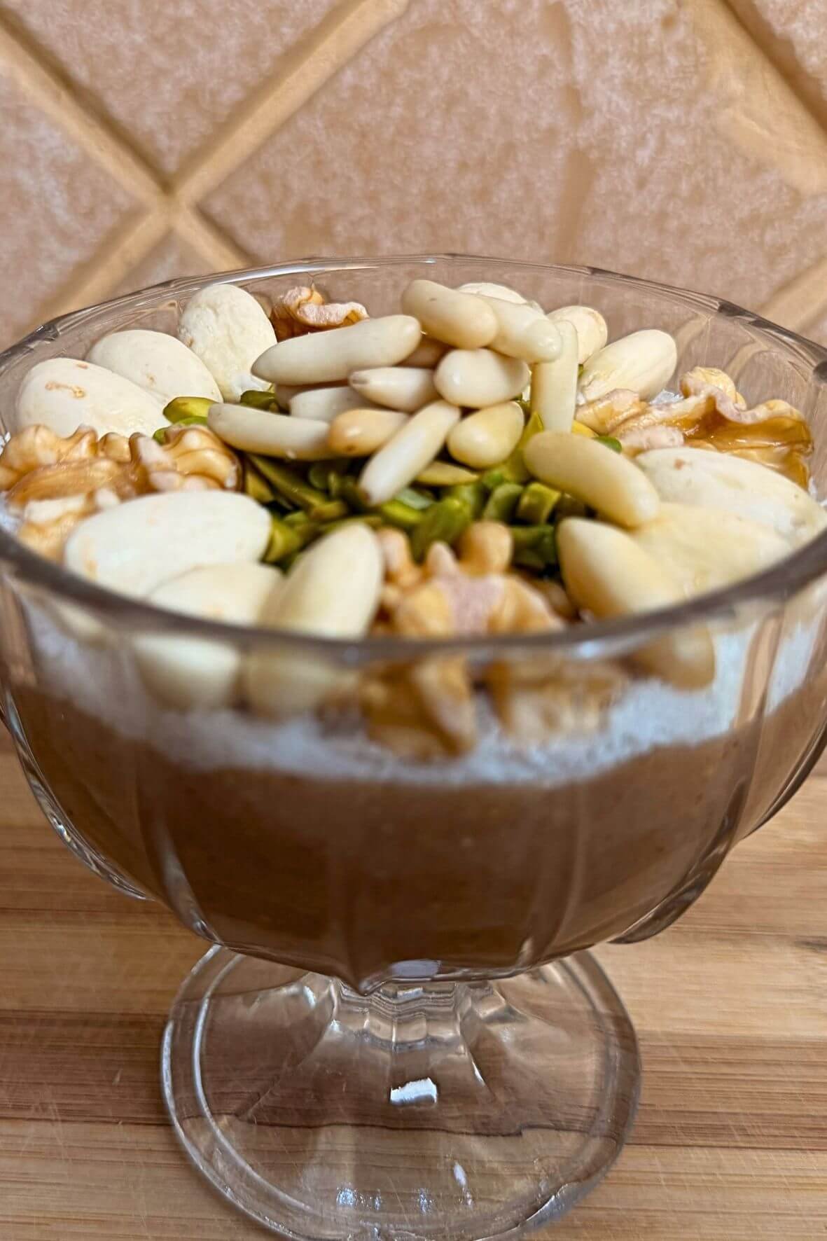 Close-up of a glass cup filled with Lebanese meghleh topped with almonds, pine nuts, pistachios, walnuts, and shredded coconut.