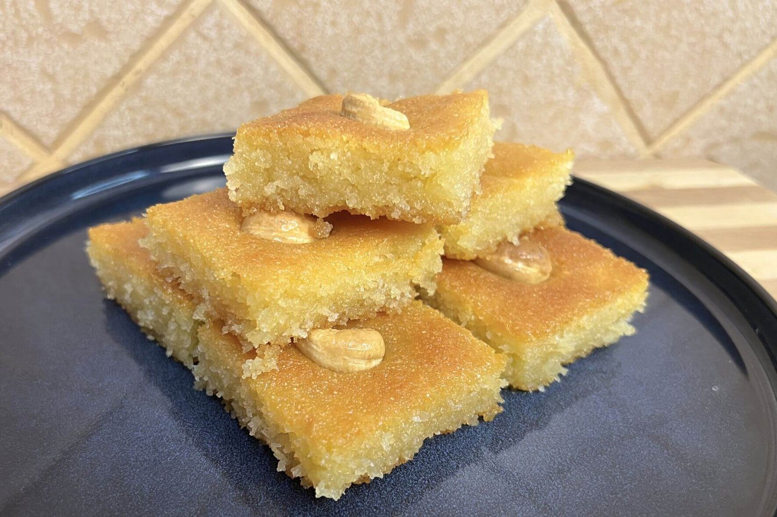 Stacked pieces of traditional Lebanese nammoura on a dark plate, golden semolina cake soaked in syrup and topped with almonds.