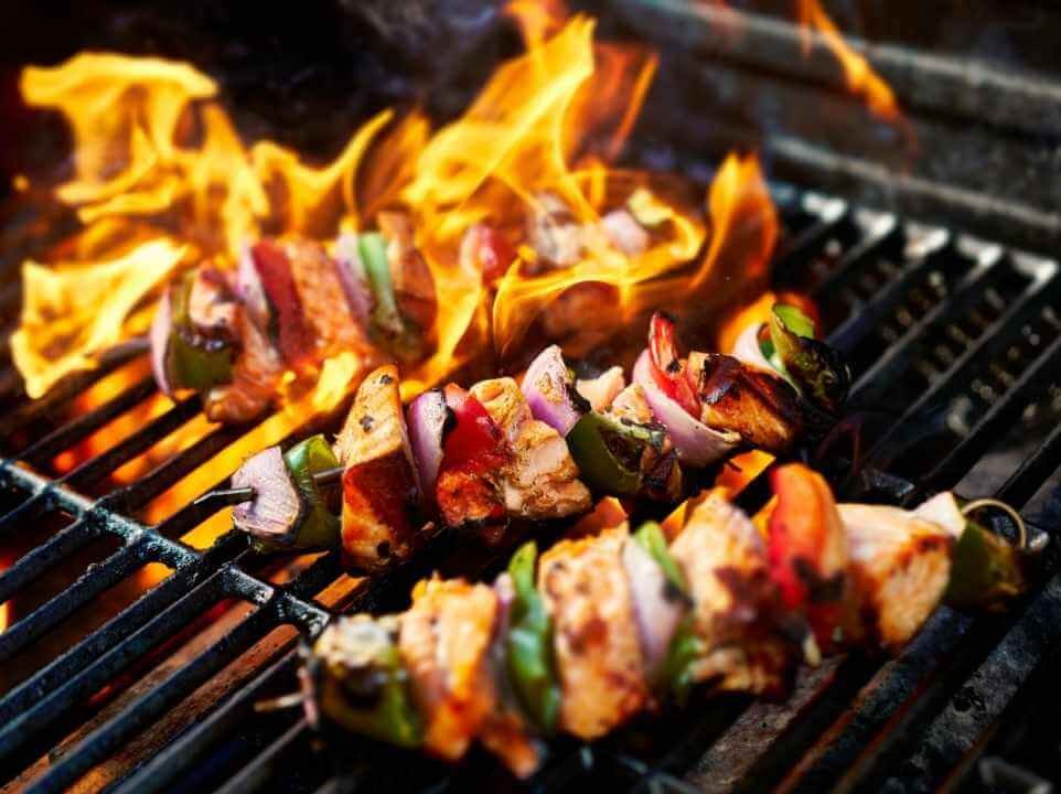 Chicken skewers with bell peppers and red onions grilling over open flames on a barbecue grill, creating a smoky charred exterior.