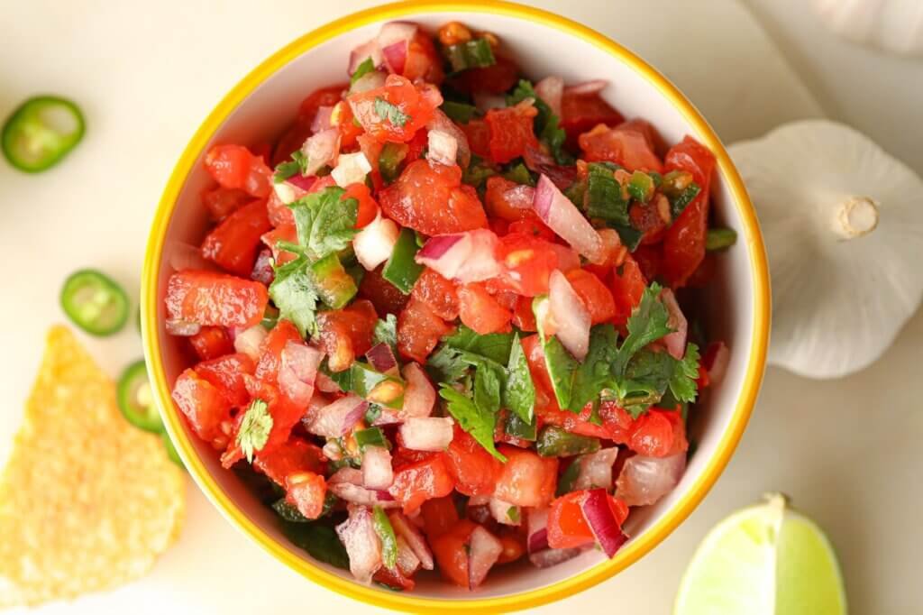 Overhead view of homemade Pico de Gallo made with diced tomatoes, red onion, jalapeños, and fresh cilantro in a bowl.