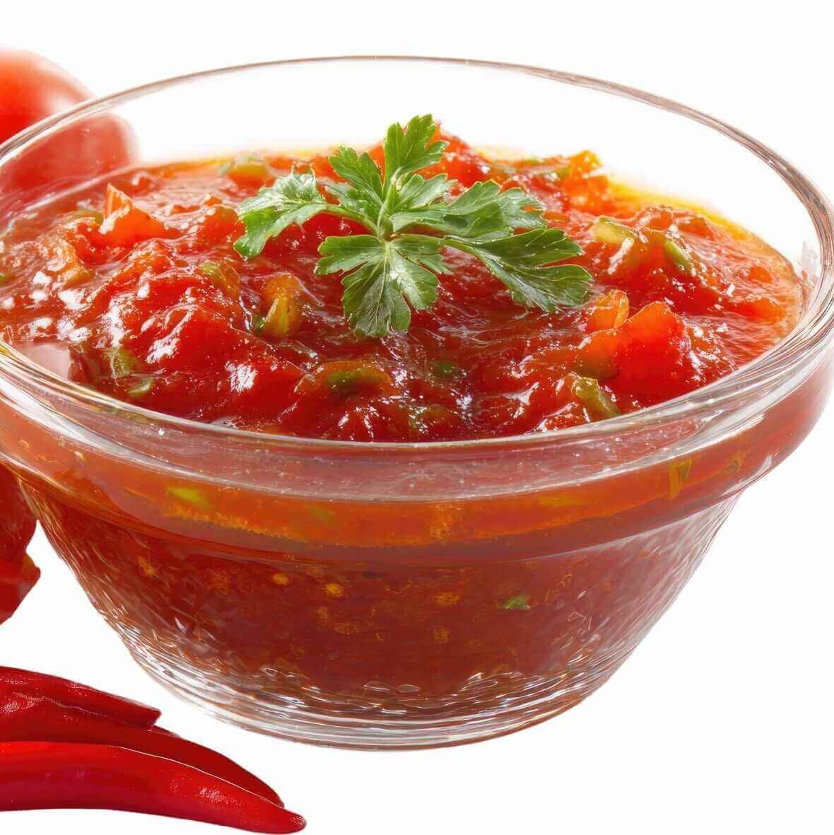Bowl of traditional red salsa made with tomatoes, chili peppers, and herbs, served alongside fresh tomatoes and red chilies.