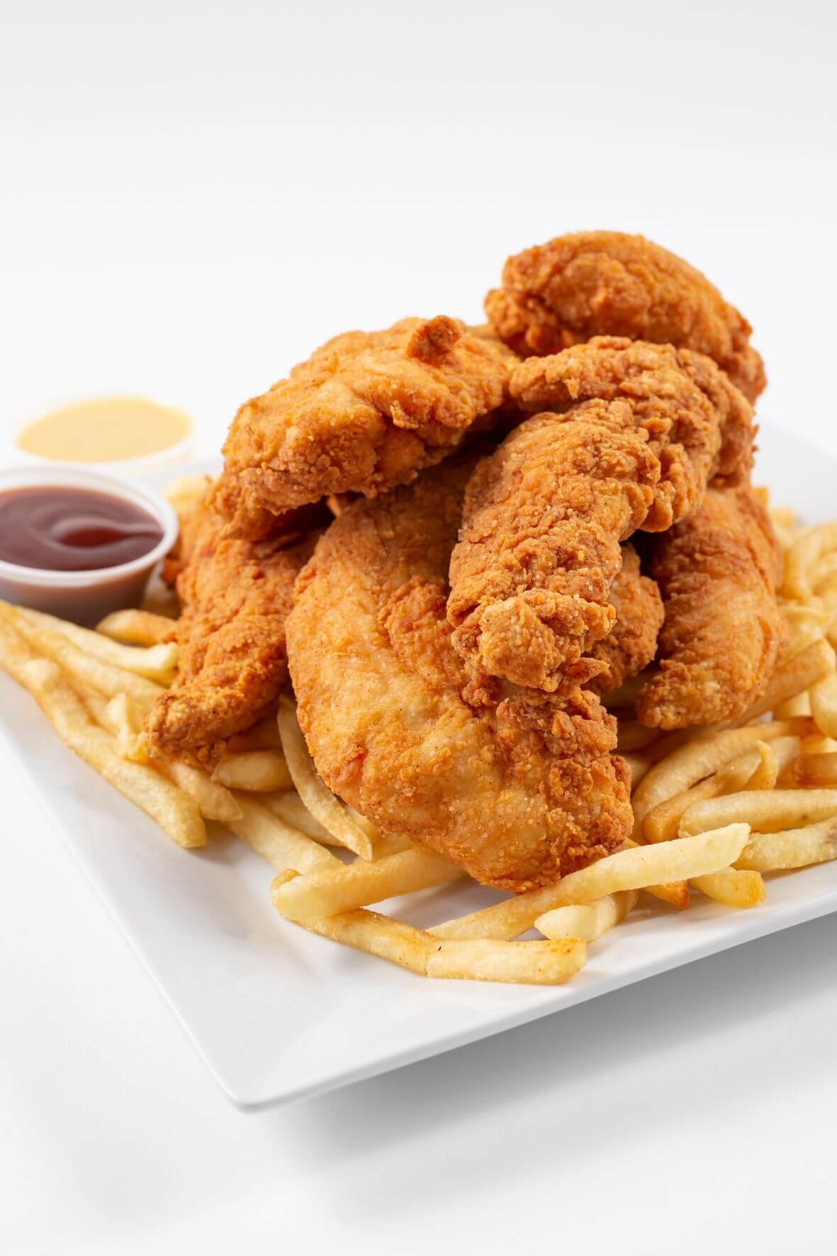 Golden crispy fish sticks served on a white plate with French fries and dipping sauces, showcasing a crunchy coating and tender fish inside.