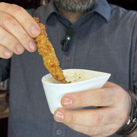 Chef François dipping a golden crispy fish stick into a bowl of creamy homemade tartar sauce.