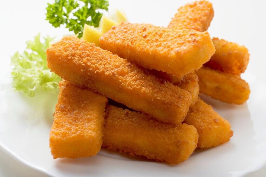 Stack of golden breaded fish fingers served on a white plate with lettuce and lemon wedges, representing the frozen fish products that became popular in Lebanon after the civil war.