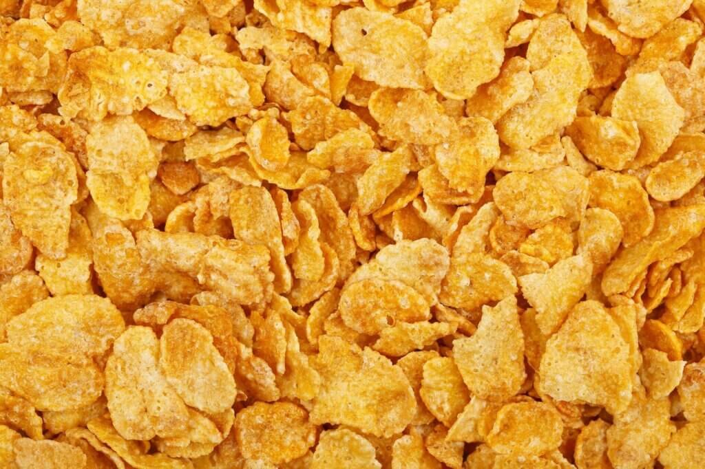 Close-up of plain cornflakes showing their crisp texture, often crushed and used as a crunchy coating for fried and baked foods.