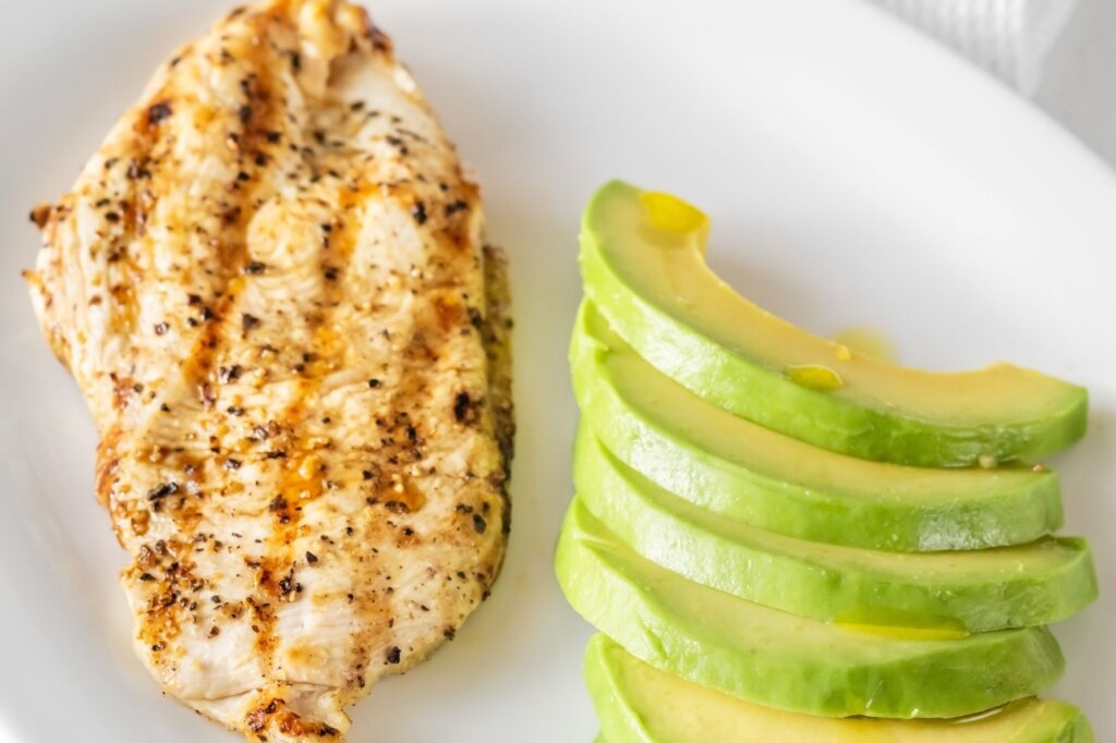 Grilled chicken breast served with fresh homemade guacamole on a white plate.