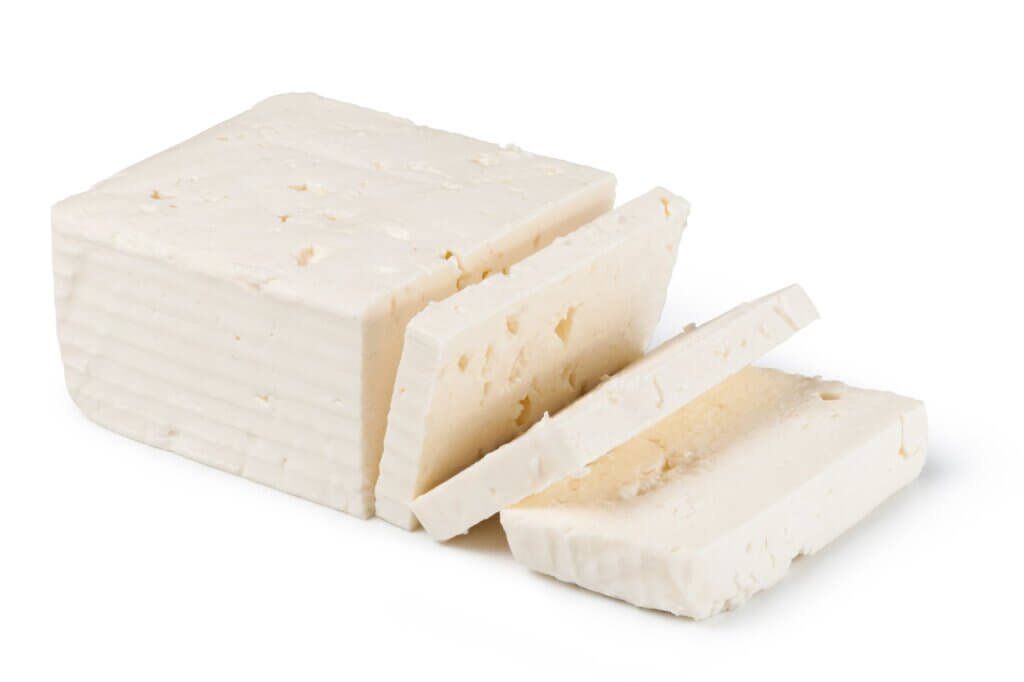 Akkawi cheese block with freshly cut slices on a white background, showing its smooth texture and firm consistency.