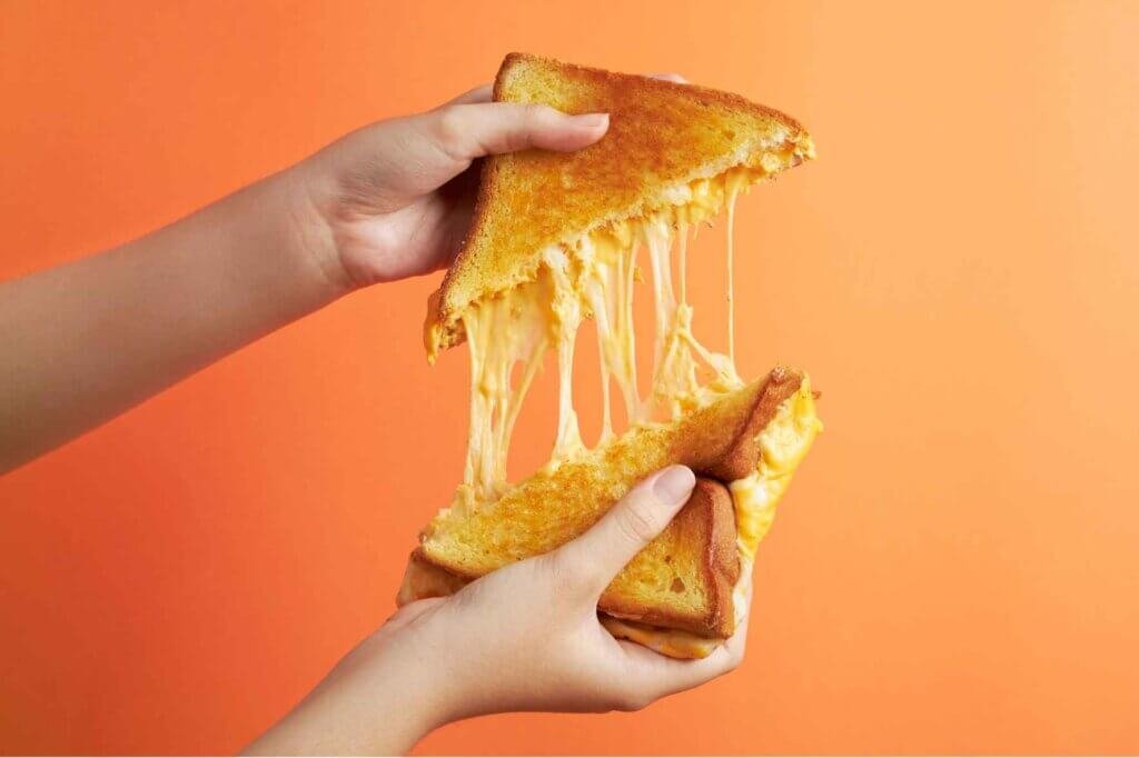 Hands pulling apart a grilled Akkawi cheese sandwich with long strands of melted Akkawi cheese stretching between the toasted bread.