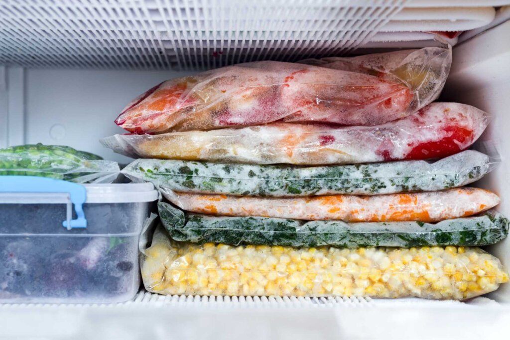 Freezer bags filled with vegetables, corn, sauces, and prepared meals stacked neatly inside a home freezer to demonstrate proper food freezing and storage.