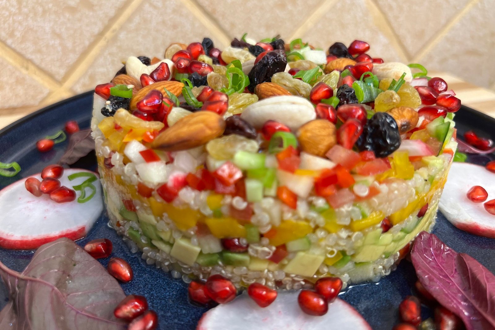Close-up of a layered quinoa salad topped with almonds, cashews, raisins, pomegranate seeds, and finely chopped fresh vegetables
