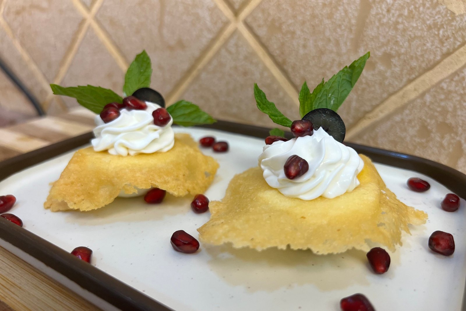 Boiled eggs topped with crispy parmesan tuile, labneh cream, pomegranate seeds, and fresh mint leaves on a white plate