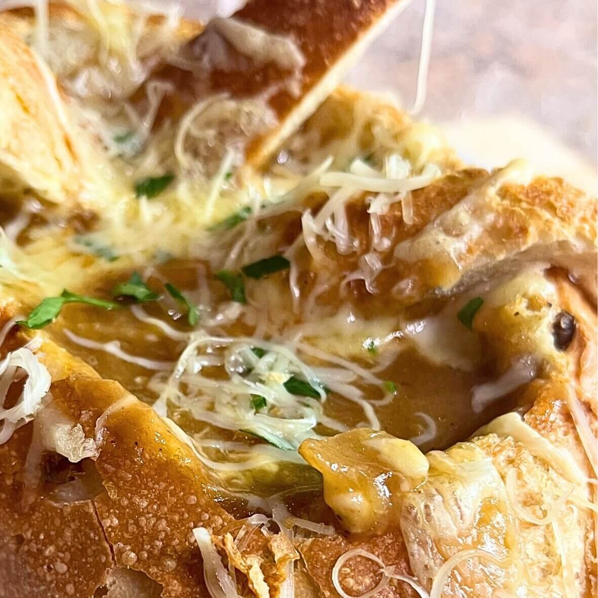Close-up of French onion soup in a crusty bread bowl with melted cheese and toasted bread lid