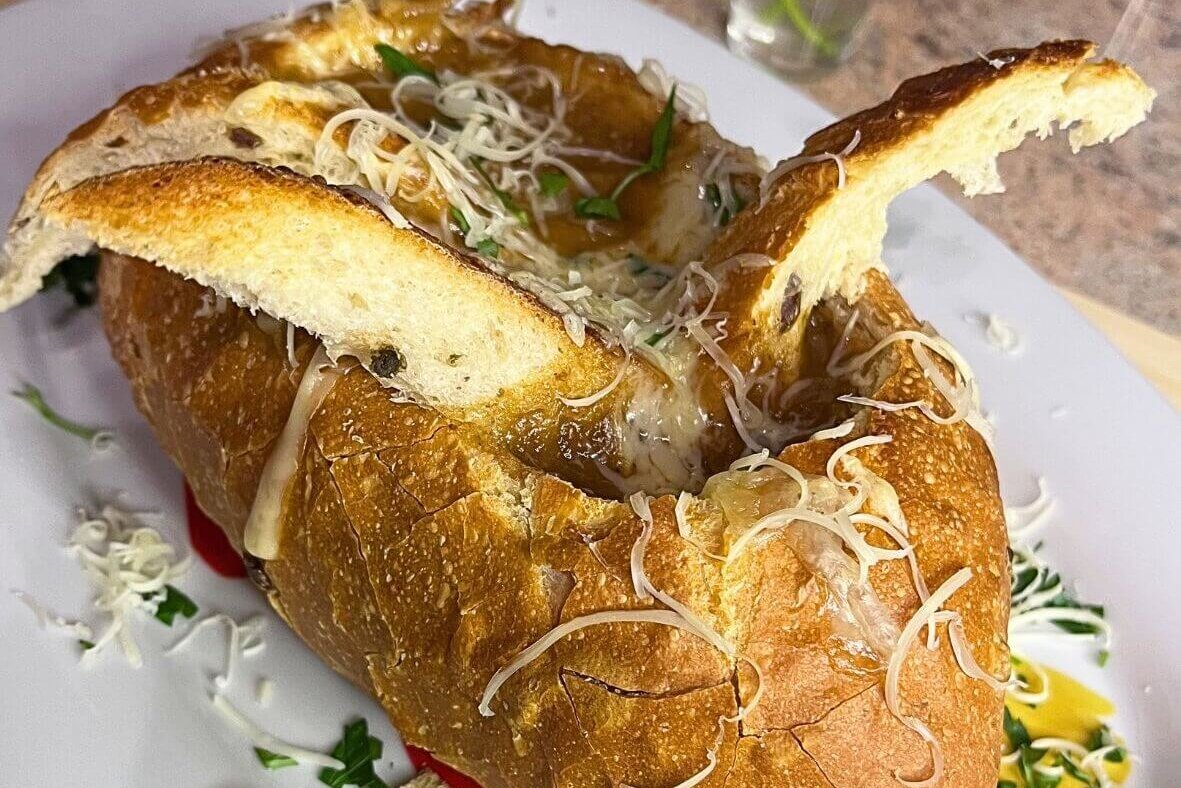 French onion soup served in a crusty bread bowl, topped with melted cheese and toasted bread slices