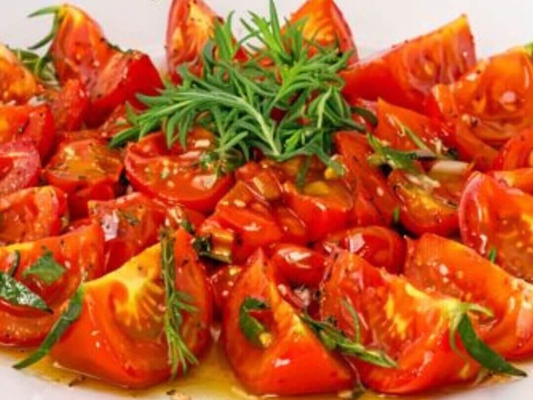 Caramelized tomatoes cut into wedges, arranged on a plate, drizzled with olive oil and garnished with fresh thyme and herbs.