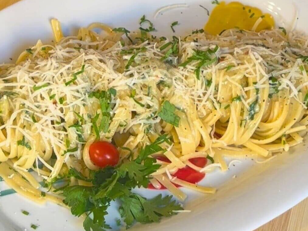 Aglio e olio linguine pasta plated with grated Parmesan cheese, fresh parsley, and cherry tomatoes on a white dish