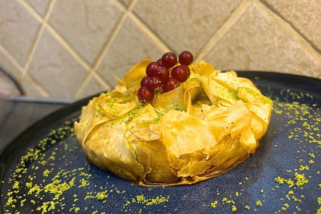 Golden Baklava Cheese Pie made with crispy phyllo pastry, a melted three-cheese filling, and garnished with ground pistachios and fresh red currants.