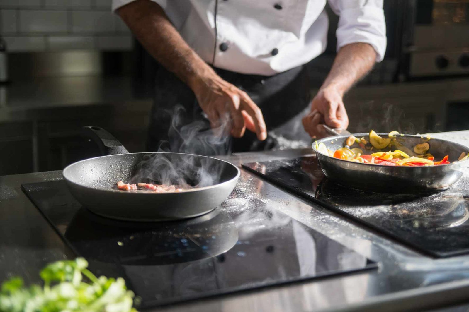 Chef François preparing fresh vegetables in a hot frying pan while cooking in a professional kitchen with steam rising from the stovetop.