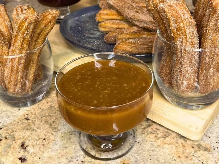 Homemade caramel sauce served in a glass dessert bowl alongside freshly made cinnamon sugar churros