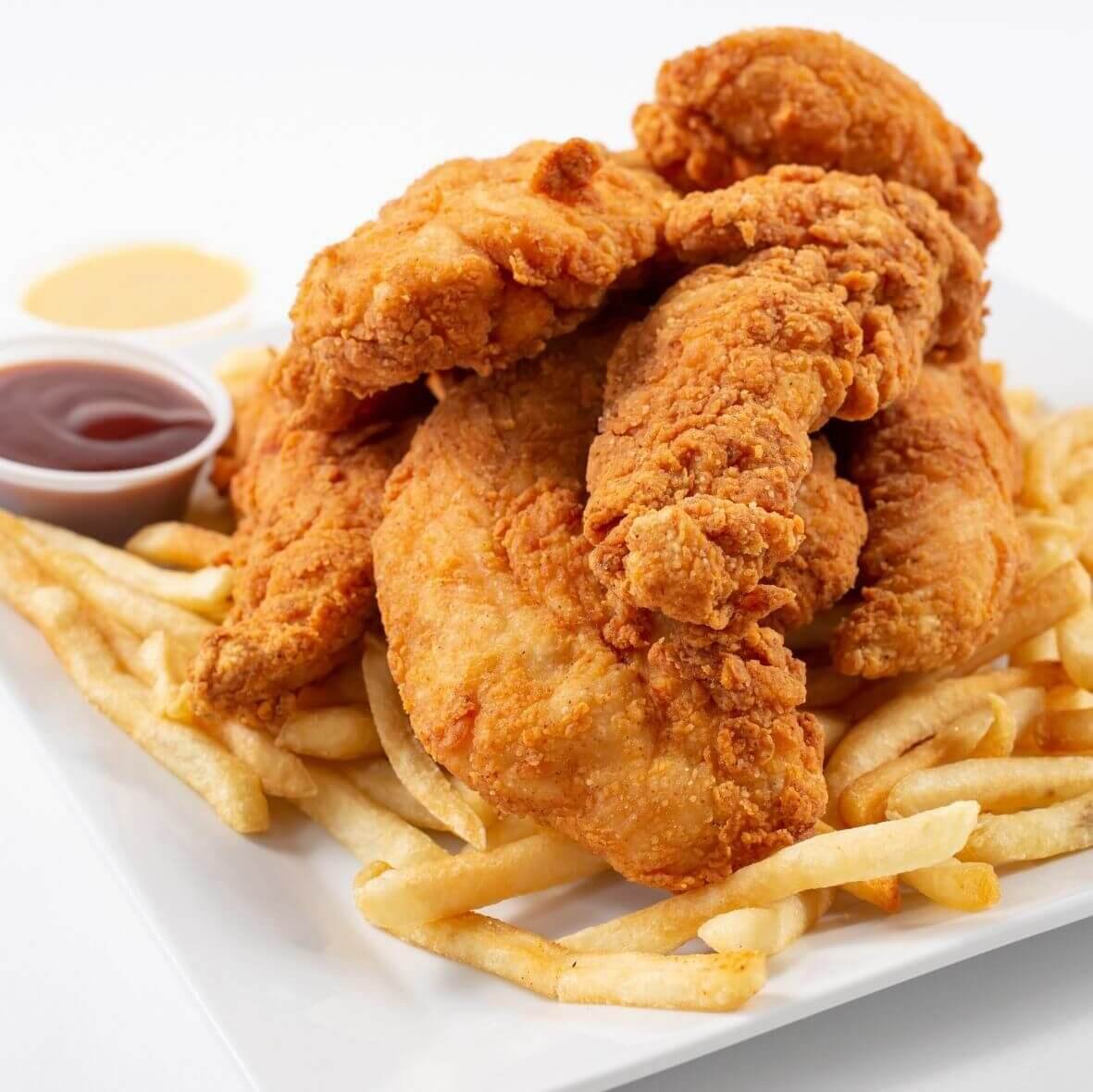 Golden crispy fish sticks served on a white plate with French fries and dipping sauces, showcasing a crunchy coating and tender fish inside.