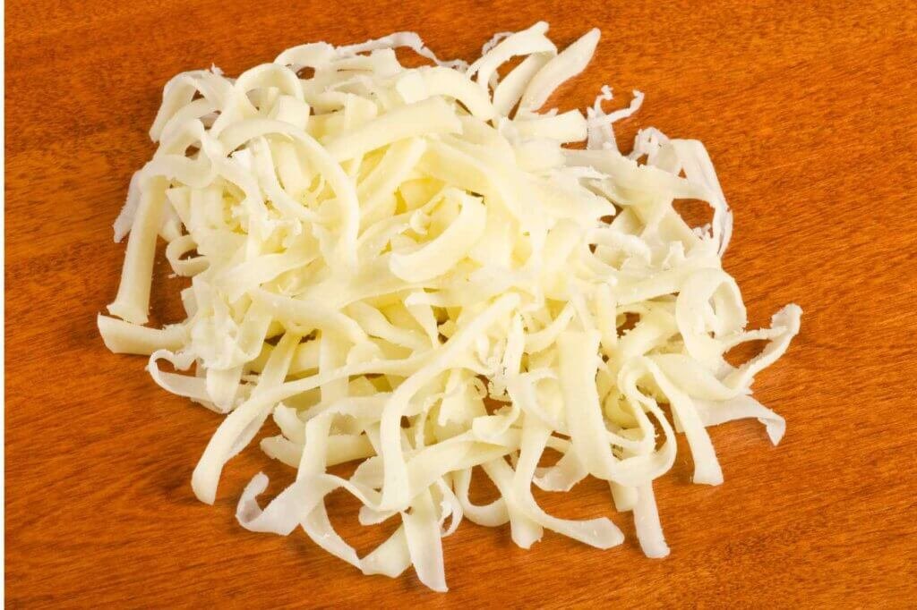 Freshly grated mozzarella cheese on a wooden board, ready to be used in a Baklava Cheese Pie recipe.