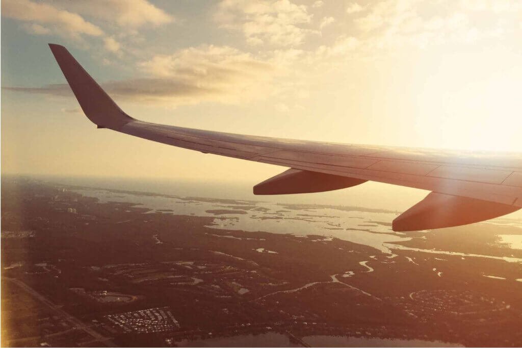 View from an airplane window showing the aircraft wing flying above the landscape during a golden sunrise.