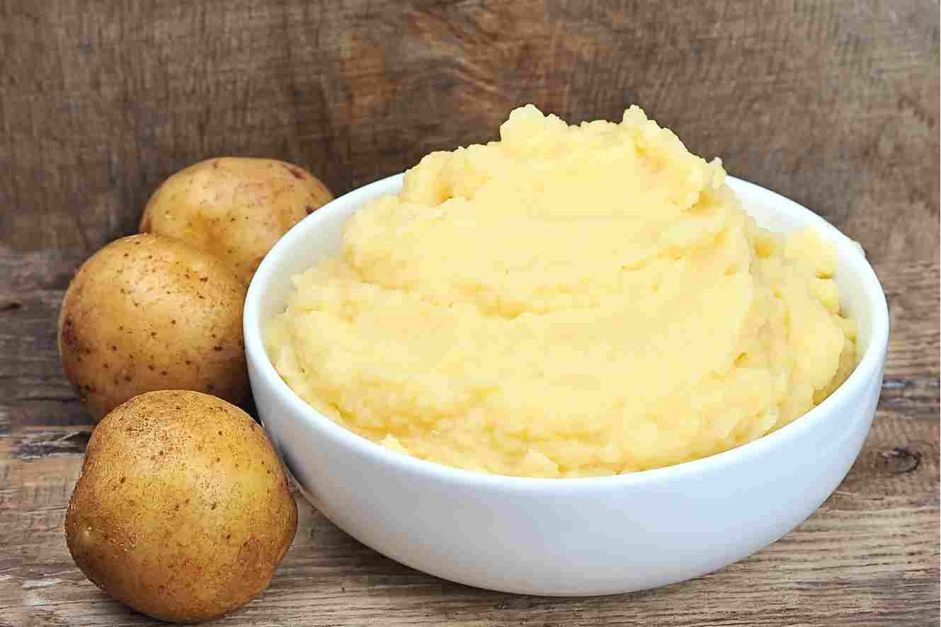 Creamy homemade mashed potato purée in a white bowl with whole potatoes.