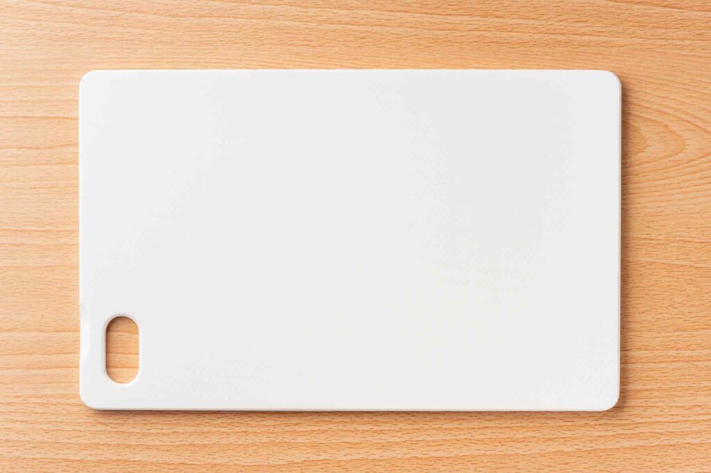 Clean white plastic cutting board placed on a wooden kitchen surface.