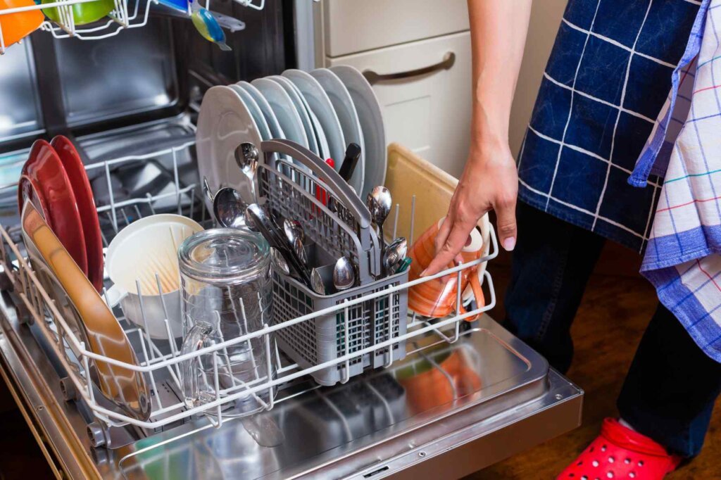 Person placing a plastic cutting board in a loaded dishwasher.