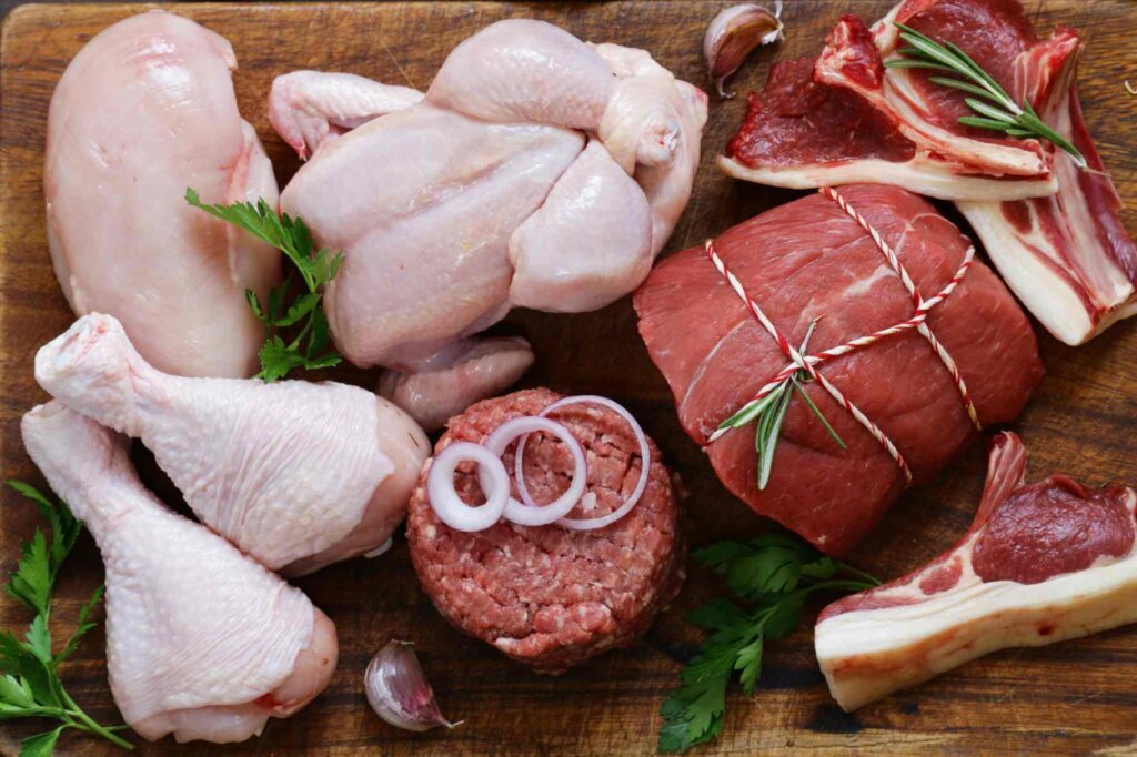 Raw chicken, minced beef, beef roast, and lamb cuts arranged on a wooden surface