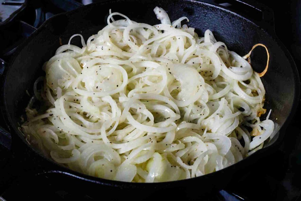 Sliced onions seasoned with salt and black pepper while cooking in a black pan.