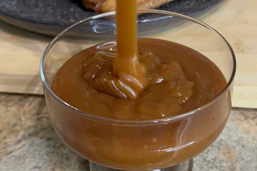 Smooth homemade caramel sauce being poured into a glass dessert bowl, perfect for dipping homemade churros.